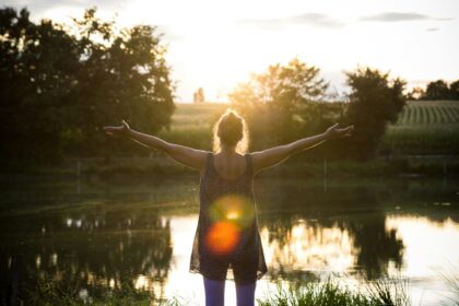 Person stands in front of a scenic pond with open arms