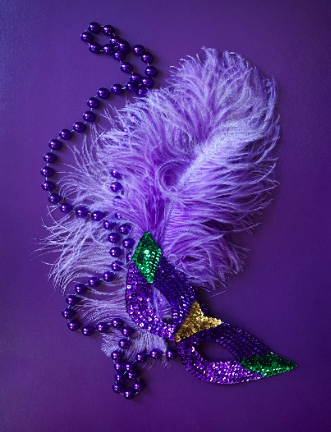 Large purple plume attached to a glittery Mardi Gras mask with purple beads on a purple background
